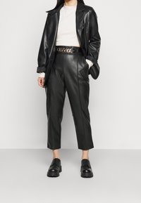 Svart läderjacka och byxor, med en kort creamfärgad tröja. Har ett kedjebälte och svarta snörskor, vilket framhäver en stilren, modern look.