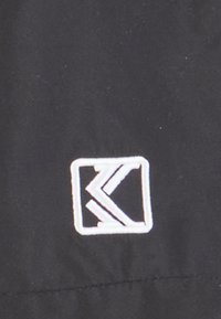 Juodas audinys su baltu siuvinėtu logotipu; logotipas yra kvadrato formos su stilizuotais raidėmis, sudarančiomis geometrinį dizainą.