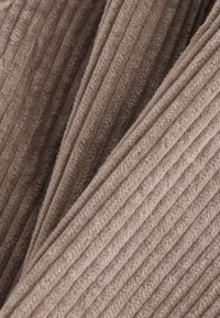 Brauner Cord-Stoff mit vertikalen Rippen, der eine weiche Textur zeigt. Die Falten erzeugen Tiefe und betonen die Plüschigkeit und Wärme des Materials.