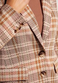 Blazer met een zigzagpatroon in tinten roze, bruin en crème. Heeft twee grote ronde knopen en een gewatteerde manchet.