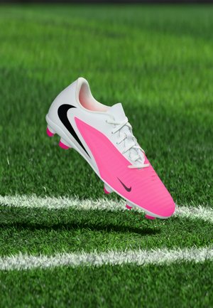 Hvid og pink Nike fodboldstøvle med sort swoosh, svævende over grøn græs nær en hvid banekant.
