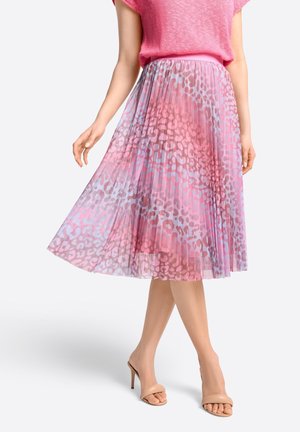 Femme portant un haut texturé rose et une jupe midi plissée à imprimé léopard rose et violet, assortie à des sandales à talons nus.