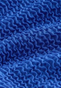 Mėlynos tekstūruotos medžiagos, kurioje matyti bangelėmis besikeičiančių raštų. Medžiaga atrodo minkšta ir lanksti, su tolygiu siuvimu ir lygiu paviršiumi.