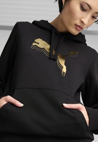 Black hooded sweatshirt with a gold Puma logo across the chest. Features a front pocket and ribbed cuffs. Smooth, soft fabric texture.