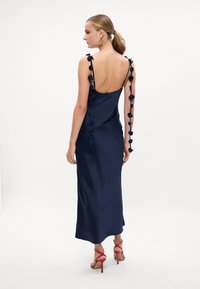 Rochie din satin bleu închis cu bretele ajustabile, accentuată cu flori din material, cu un decolteu în spate adânc și croială ajustată, asortată cu sandale cu toc roz.