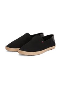 Zapatillas de lona negras tipo slip-on con suela de yute trenzado, que presentan un diseño minimalista y un pequeño logo en tricolor en el lateral.