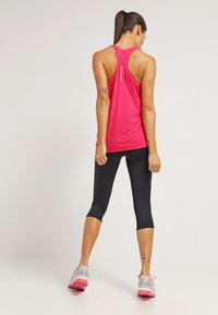 Top deportivo rosa con diseño de espalda nadadora, combinado con leggins capri negros y zapatillas para correr gris-rosa, presentando una textura suave.
