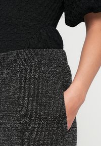 Top preto texturado combinado com uma saia salpicada em preto e branco, apresentando um bolso lateral, destacando tecidos e padrões contrastantes.