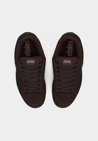 Ζευγάρι σκουροκάστανα αθλητικά παπούτσια Etnies με κορδόνια, σε θέα από πάνω σε λευκό φόντο.