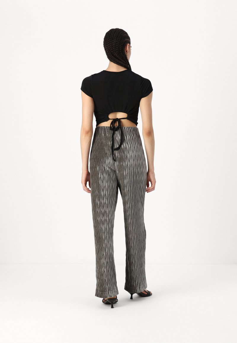 Schwarzes, kurz geschnittenes Oberteil mit geknotetem Rücken, kombiniert mit grauen, weit geschnittenen Hosen mit einem strukturierten Zickzackmuster.