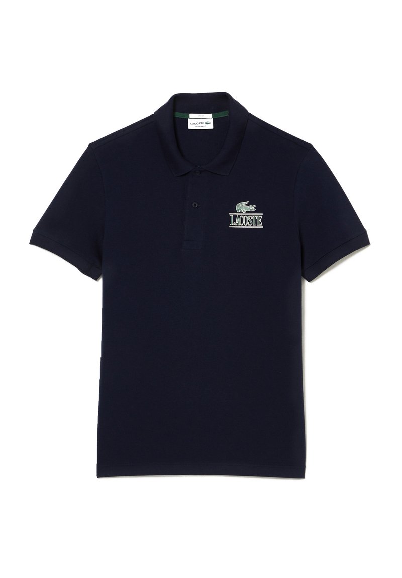 Polo de color azul marino hecho de algodón, con cuello, mangas cortas y un logo bordado de cocodrilo verde con el texto "LACOSTE".