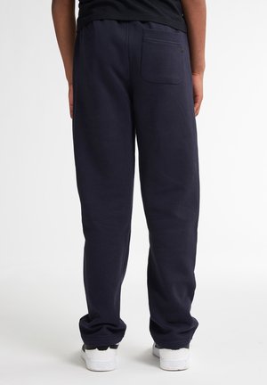 Pantaloni tuta blu navy con una vestibilità comoda, realizzati in tessuto morbido, dotati di una tasca posteriore e una vita a costine, abbinati a sneakers bianche.