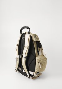 Schwarzer und beiger Rucksack mit gepolsterten Trägern, verstellbaren Seitentaschen, Reißverschlussverschlüssen und strukturierter Oberfläche. Robuster Griff oben.