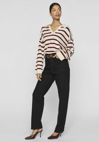 Gestreifter Pullover in Creme und Bordeaux mit V-Ausschnitt und Kragen, kombiniert mit hoch sitzenden schwarzen Jeans und Bordeaux-farbenen High-Heels.