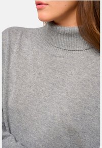 Pull à col roulé gris avec texture côtelée et un col ajusté. Matériau doux et coupe décontractée visibles en vue raccourcie.
