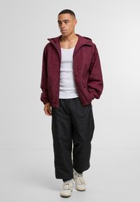 Burgundijas krāsas zip-up jaka ar teksturētu apdari; valkāta virs baltas bezrūpīgas topa un saskaņota ar brīviem melniem biksēm un baltām kedām.