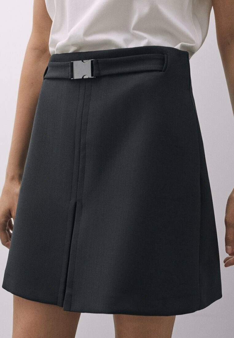 Jupe noire avec taille cintrée ornée d'une boucle argentée, tissu taillé sur mesure, devant plissé et bas évasé, conçue pour une silhouette structurée.