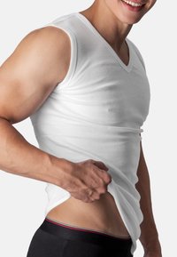 White, sleeveless V-neck shirt made of smooth fabric, fitted around the torso, showcasing a muscular build. Black waistband with red accents visible.