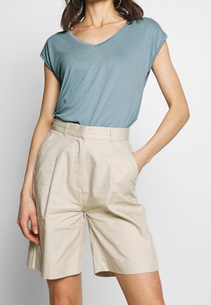 Lichtblauw T-shirt met V-hals en opgerolde mouwen, gecombineerd met beige shorts met hoge taille. De outfit heeft een gladde stoftextuur en een losse pasvorm.