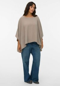 Heledbeez, suur suurusega poncho topp ümmarguse kaeluse ja voogava disainiga. Koos siniste laia säärega teksade ja mustade mustritega kingadega.