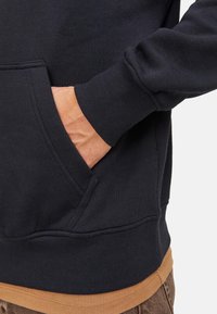 Schwarzer Sweatshirt aus Baumwollmischung, mit einer Brusttasche, gerippten Bündchen und einem eingearbeiteten hellbraunen Saum. Glatte Textur mit subtilen Nähdetails.