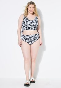 Bikini-Set mit Schwarz-Weiß-Palmenmuster, bestehend aus einem cropped Top mit Bindebändern und hochgeschnittenen Bottoms, kombiniert mit Sandalen mit offenen Zehen.