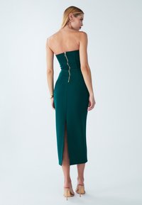 Teal strapless midi mekko, jossa on tiukka yläosa, takana vetoketju ja halkio. Silkkinen pinta, tyylikäs muotoilu ja elegantti siluetti.