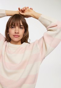 Sweter wykonany z dzianiny w kolorze kremowym z poziomymi różowymi paskami. Posiada łódź dekolt oraz lekko bufiaste rękawy, prezentując miękką teksturę.