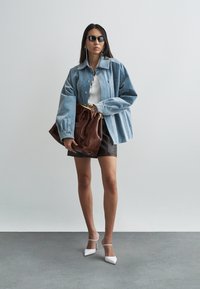 Spijkerjack, witte nauwsluitende top, zwarte minirok en bruine leren tas. Witte sandalen met hak. Donkere zonnebril, lang donker haar en een eenvoudige oorbel.