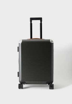 Valise rigide vert foncé avec quatre roues et une poignée télescopique noire étendue sur fond blanc.