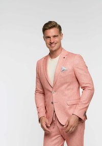 Svijetlopink žaket od teksturirane tkanine s dvostrukim kopčanjem, prsni džep s sivoj maramicom, uparen s krem majicom.