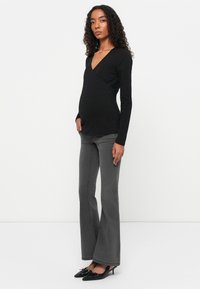 Top avvolgente nero a maniche lunghe sopra jeans grigi a zampa d'elefante, caratterizzato da una texture liscia e un design semplice. Indossato con scarpe nere con tacco.