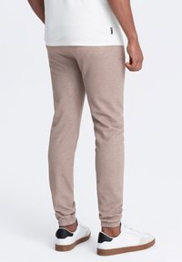 Jasnobrązowe dresy z teksturowanym wykończeniem, dopasowane mankiety, w połączeniu z białymi sneakersami z czarnymi akcentami i beżowymi podeszwami.