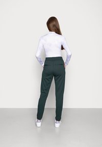 Long-sleeve lavender top with cloud pattern, paired with dark green tapered pants featuring an elastic waistband and back pockets. White sneakers.