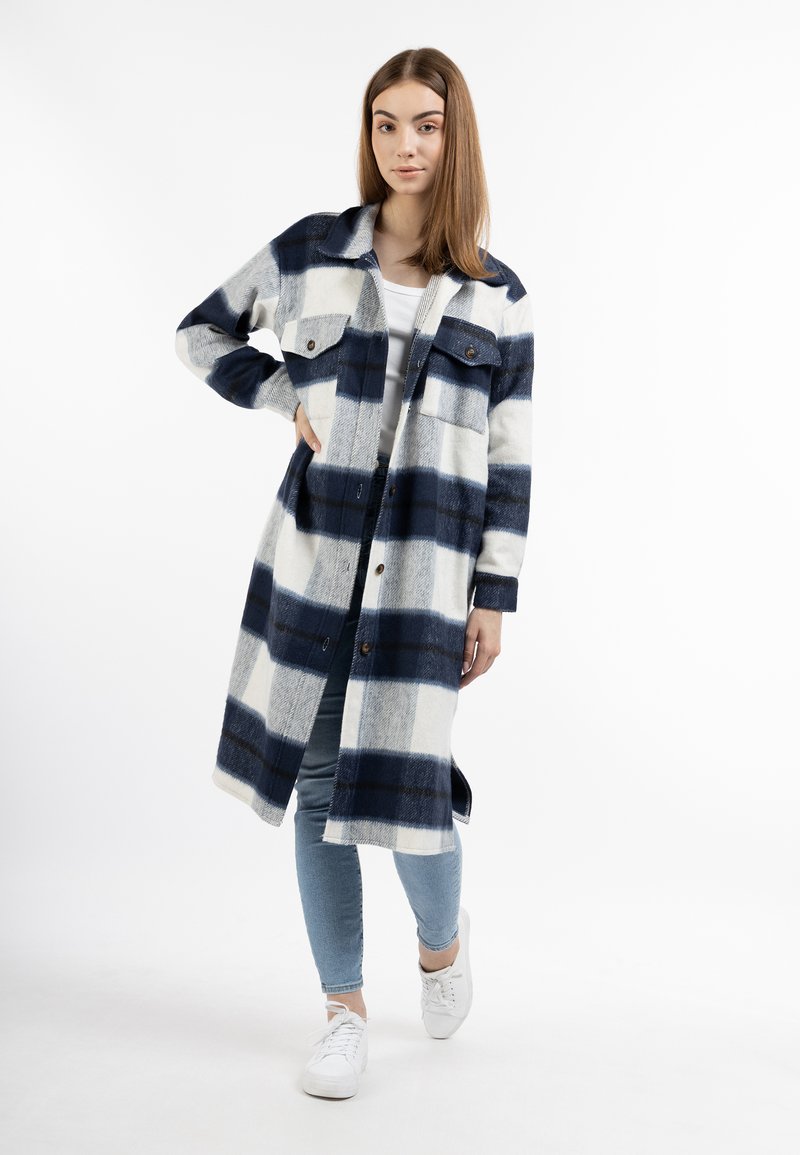 Cappotto a quadri blu e bianco con bottoni, dotato di due tasche sul petto, maniche lunghe e una vestibilità comoda, abbinato a jeans azzurri e sneaker bianche.