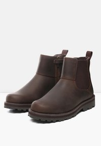 Botas de tobillo de cuero marrón con paneles laterales de elastano, puntera redonda y suela con textura. Incluyen un zipper lateral para facilitar su uso.