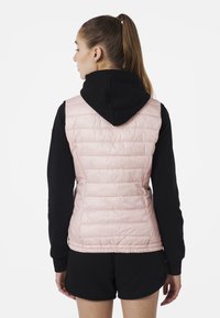 Světle růžový prošívaný vestu s prešíváním, pod ním černá mikina s kapucí, pohled zezadu, hladká textura, těsný střih.