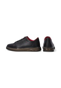 Schwarze Leder-Sneaker mit abgerundetem Zehenbereich, rotem Innenfutter und einer strukturierten braunen Gummisohle mit Wellenmuster.