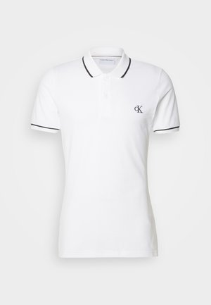 Polo shirt bianco in cotone, con un bordo nero sul colletto e sulle maniche, e un piccolo logo CK sul lato sinistro del petto.