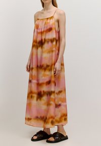Maxi-jurk met spaghettibandjes, featuring een roze en bruine tie-dye patroon, gladde stof en een relaxte pasvorm. Draagt met bruine slip-on sandalen.