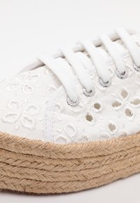 Hvide snørebåndssneakers med broderede blomsterdesigns, øjenlågudskæringer og en seneproppet kilebund. Glat stoftekstur med metallic accenter.