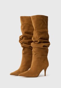 Bottes à talons hauts marron en daim, décontractées, avec des pointes émoussées, présentant une texture douce et des détails froncés au niveau de la tige.