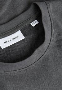 Col de chemise gris foncé à col rond avec une étiquette de marque blanche indiquant Jack & Jones et une étiquette plus petite indiquant Made in Bangladesh.