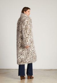 Płaszcz ze sztucznego futra o długim, luźnym kroju z mieszanką beżowych i brązowych wzorów. Połączony z dzwonowatymi jeansami i brązowymi botkami na obcasie.