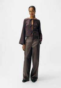 Geruite blouse met lange mouwen heeft een voorste striksluiting, gecombineerd met wijde, glanzende bruine broek. Platte zwarte schoenen maken de look compleet.