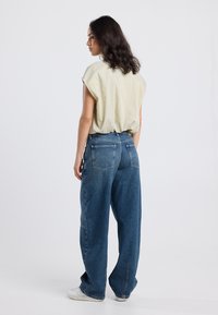 Light yellow, striped blouse with cap sleeves paired with oversized, blue denim jeans. The jeans feature a back pocket design and a relaxed fit.