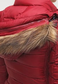 Chaqueta de plumas roja con capucha acentuada con pelo, que presenta un acabado suave y brillante, paneles laterales acanalados y un zipper en contraste.