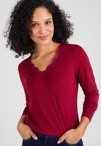 Bordeaux langemouwshirt met een V-hals en verfijnde kantafwerking rond de halslijn, gemaakt van zachte, gladde stof.