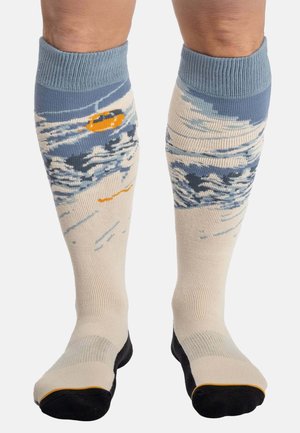 Beige und blaue knielange Socken mit Wellenmuster; elastischer gerippter Bund, verstärkte schwarze Fußspitze und Ferse, mit einem orangefarbenen Akzent.