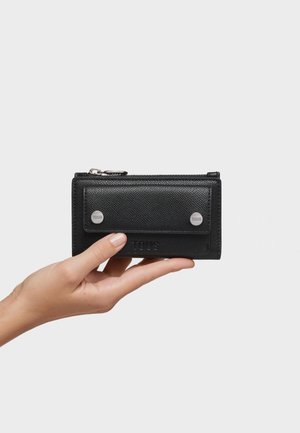 Hand holding a black textured leather wallet with front flap secured by two silver buttons on light gray background.